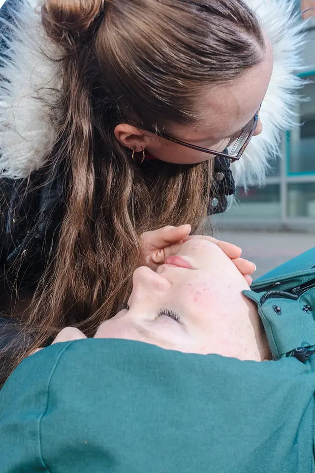 Erste Hilfe im Freien: Eine Ersthelferin überprüft Atmung und Bewusstsein einer regungslos am Boden liegenden Person.